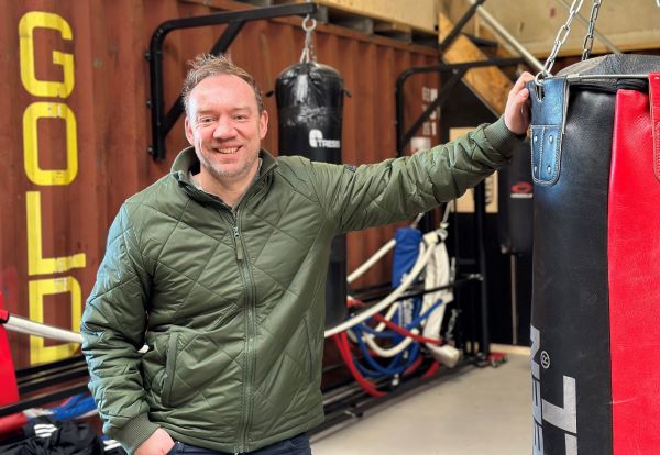 Skolelederen står i et crossfitlokale med armen på en boksepude.